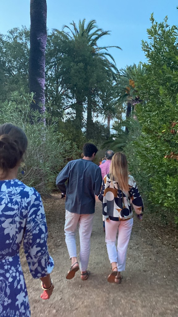 Un public amateur s'avance dans une allée de grands palmiers, celle du Château de La Moutte, à Saint-Tropez