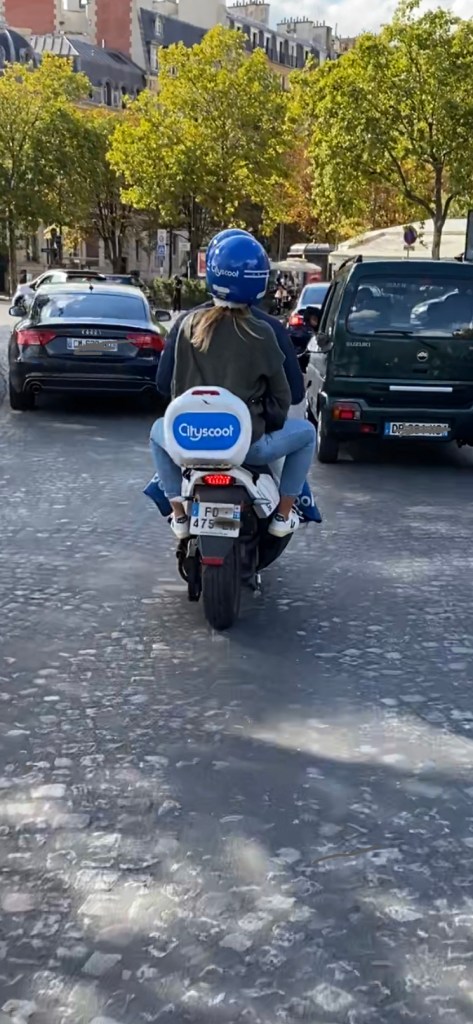 Un city Scoot électrique avec 2 personnes dessus tentent de se frayer un chemin entre les voitures Place du Trocédéro.