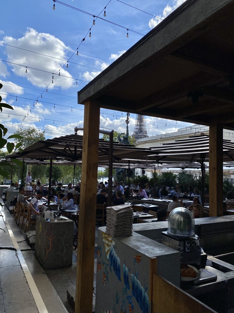 les tables extérieures du restaurant sont toutes bie remplies de convives sous un joli ciel bleu.